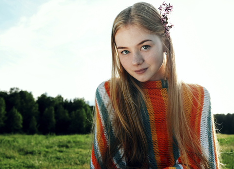 Porträt einer selbstbewussten Frau mit Blumen auf einem Feld gegen den Himmel, lizenzfreies Stockfoto