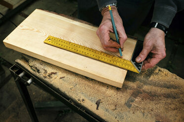 Cropped hands of carpenter measuring wooden plank in workshop - CAVF34321
