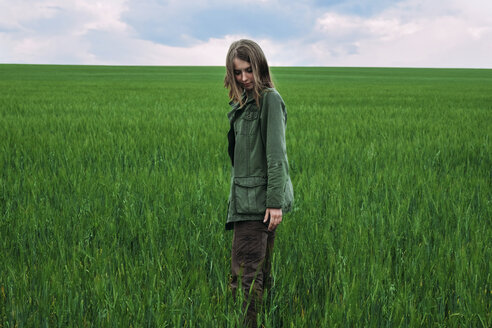 Frau stehend auf grasbewachsenem Feld gegen bewölkten Himmel - CAVF34335