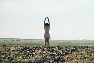 Rückansicht einer Frau, die sich im Stehen auf einem felsigen Feld gegen den klaren Himmel streckt - CAVF34347