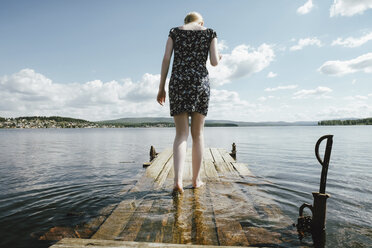 Rear view of woman walking on pier in river against cloudy sky - CAVF34348