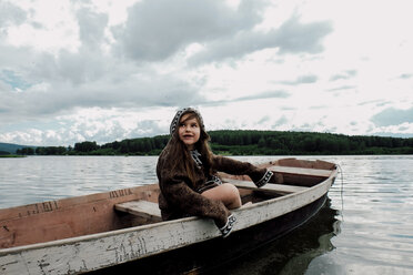 Girl looking away while sitting in rowboat on lake against cloudy sky - CAVF34357