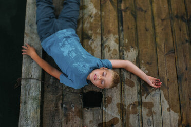 Overhead view of boy lying on wooden pier - CAVF34361