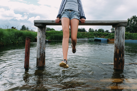 Tiefschnitt eines Teenagers, der auf einer Bank über einem See sitzt und mit Wasser spielt, lizenzfreies Stockfoto