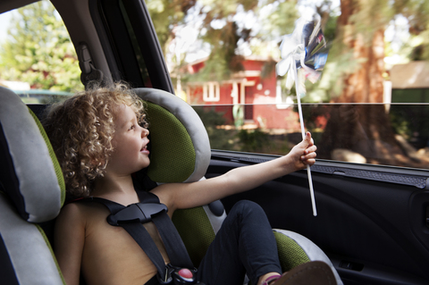 Glückliches Mädchen, das ein sich drehendes Windrad betrachtet, während es im Autositz sitzt, lizenzfreies Stockfoto