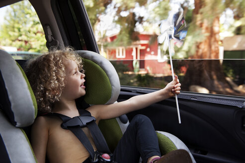 Glückliches Mädchen, das ein sich drehendes Windrad betrachtet, während es im Autositz sitzt - CAVF34414