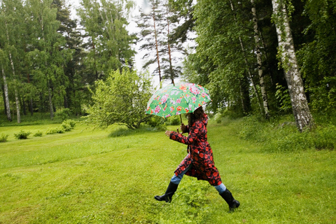 Frau mit geflecktem Regenmantel geht in einem Feld spazieren, lizenzfreies Stockfoto