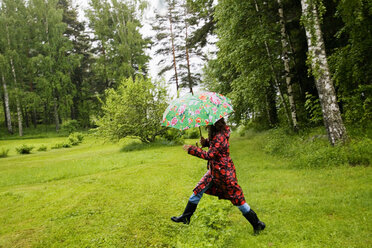 Woman wearing spotted raincoat walking in field - FOLF09191