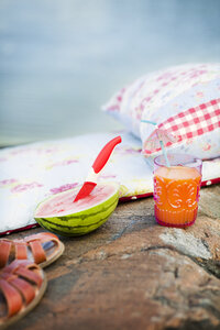 Kissen, Sandalen, Wassermelone und ein Glas Saft auf einem Felsen - FOLF09258