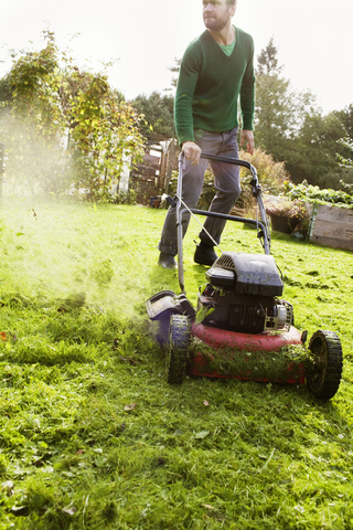 Mann mäht Rasen im Hausgarten, lizenzfreies Stockfoto