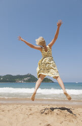 Woman jumping on beach, looking at Bay of Biscay in Spain - FOLF09412