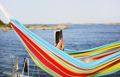 Man lying in hammock and reading book - FOLF09548