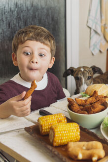 Boy with dog enjoying american food at dining table at home - SKCF00393
