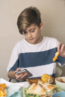 Junge isst am Esstisch und schaut gleichzeitig auf das Telefon - SKCF00396
