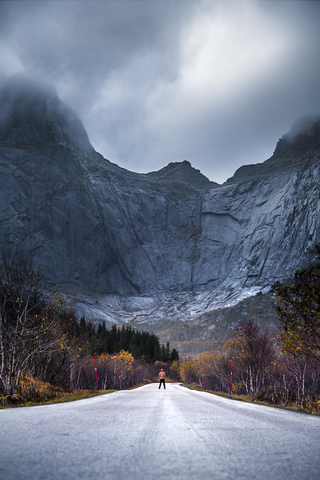 Norwegen, Lofoten-Inseln, Mann steht auf leerer Straße umgeben von einer Felswand, lizenzfreies Stockfoto