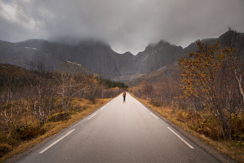 Norwegen, Lofoten-Inseln, Mann steht auf leerer Straße umgeben von einer Felswand - WVF00945