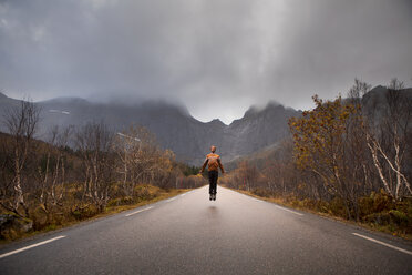 Norway, Lofoten Islands, man jumping on empty road surrounded by rock face - WVF00946