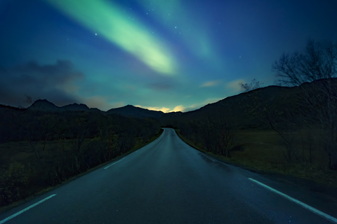 Norwegen, Lofoten-Inseln, Nordlicht über leerer Straße, lizenzfreies Stockfoto