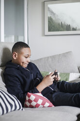 Teenage boy using mobile phone on sofa in living room - MASF00027
