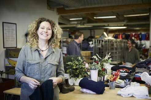 Portrait of smiling mature woman standing against colleagues working in warehouse - MASF00033