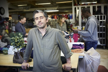 Portrait of confident mature man standing against colleagues working in warehouse - MASF00034