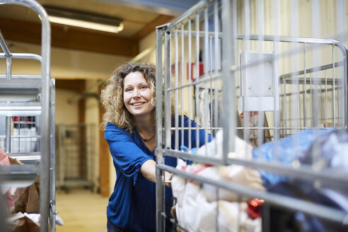 Smiling mature female volunteer pushing cart while looking away at warehouse - MASF00060