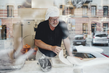Älterer männlicher Bäcker, der in einer Bäckerei steht und sein Buch kontrolliert - MASF00083