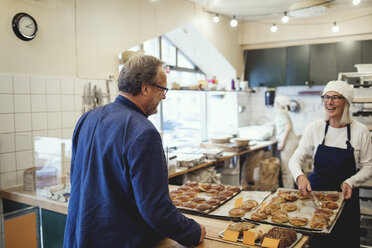 Lächelnde Besitzerin zeigt Kunden in einer Bäckerei frisch gebackene Lebensmittel - MASF00093