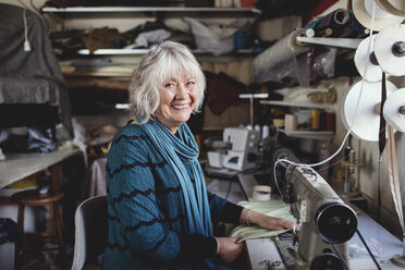 Porträt einer lächelnden Seniorin an der Nähmaschine in der Werkstatt - MASF00116