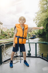 Selbstbewusster Junge, der ein Boot im Fluss gegen den Himmel steuert, in voller Länge - MASF00131