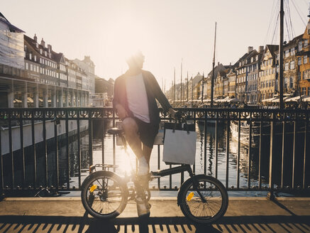 Mann mit Fahrrad und Einkaufstaschen auf einer Fußgängerbrücke in der Stadt in voller Länge von hinten beleuchtet - MASF00140