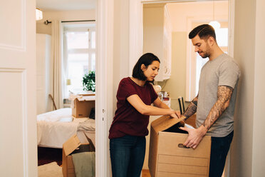 Woman unpacking box held by man in corridor at new home - MASF00148