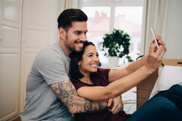 Glückliches Paar, das ein Selfie mit dem Handy macht, während es sich im Schlafzimmer ausruht - MASF00157