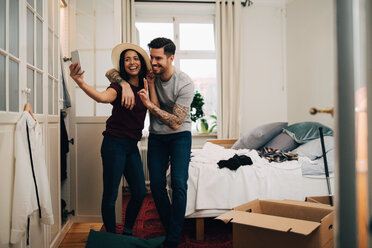Smiling couple taking selfie on mobile phone while standing in bedroom - MASF00162