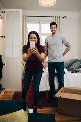 Woman taking selfie on mobile phone while standing with man in bedroom - MASF00166