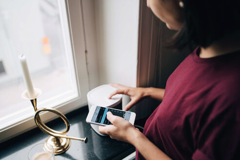 Midsection of woman using smart phone while standing by window - MASF00176