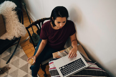 High angle view of woman having tea while using laptop by wall - MASF00184