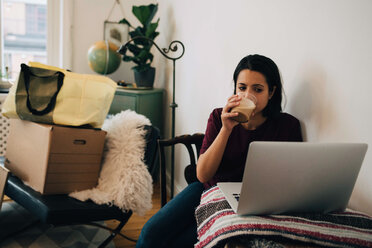 Frau trinkt Tee, während sie einen Laptop an der Wand benutzt, während sie ihr Haus umzieht - MASF00185