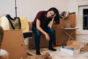 Portrait of smiling woman sitting on cardboard box at home - MASF00192