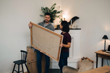 Man and woman looking at painting while standing by fireplace in living room - MASF00193