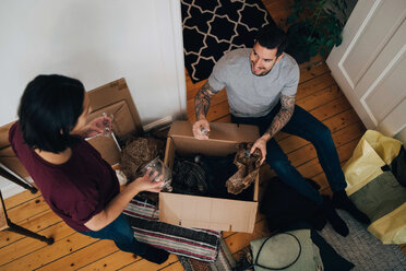 High angle view of man and woman unpacking box in living room - MASF00196