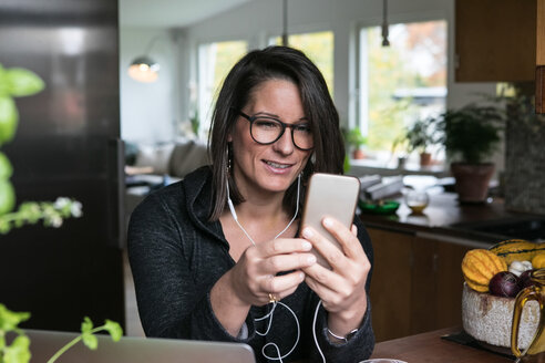 Weibliche Designerin benutzt ein Mobiltelefon, während sie in ihrem Büro sitzt - MASF00225