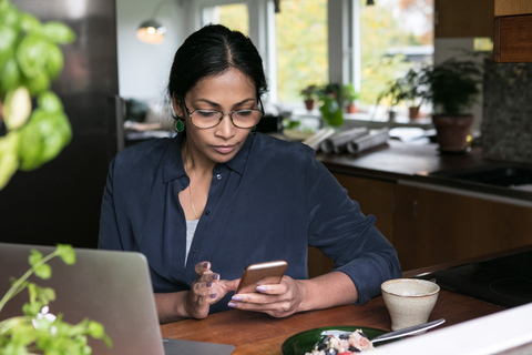Geschäftsfrau mit Mobiltelefon und Laptop auf dem Tisch im Heimbüro, lizenzfreies Stockfoto