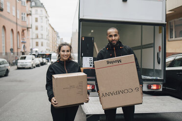 Porträt von männlichen und weiblichen Arbeitern, die Kisten tragen, während sie vor einem Lieferwagen in der Stadt stehen - MASF00234