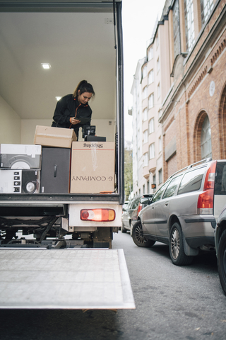 Mitarbeiterin mit digitalem Tablet bei der Analyse von Paketen im Lieferwagen in der Stadt, lizenzfreies Stockfoto