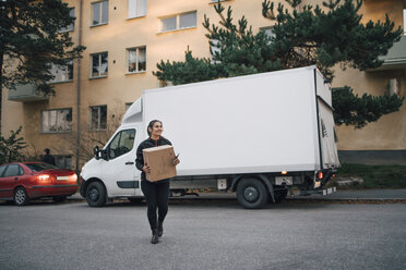 Weiblicher Arbeiter in voller Länge, der eine Kiste trägt, während er auf der Straße gegen einen Lieferwagen läuft - MASF00247