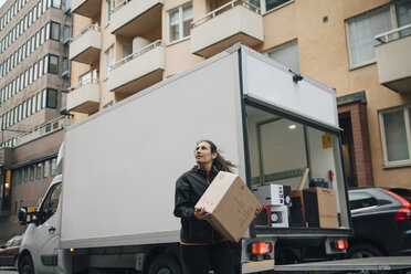 Frau, die eine Kiste trägt, während sie neben einem Lieferwagen in der Stadt steht - MASF00249