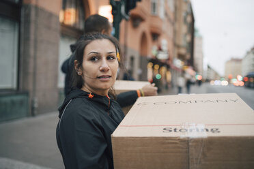 Nachdenkliche Frau, die eine Schachtel trägt, während sie mit einem Mitarbeiter in der Stadt spazieren geht, während einer Lieferung - MASF00250