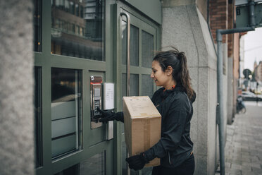 Female messenger ringing intercom on closed door while carrying box on sidewalk - MASF00253