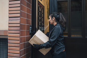 Female messenger ringing intercom while carrying box by closed door - MASF00255